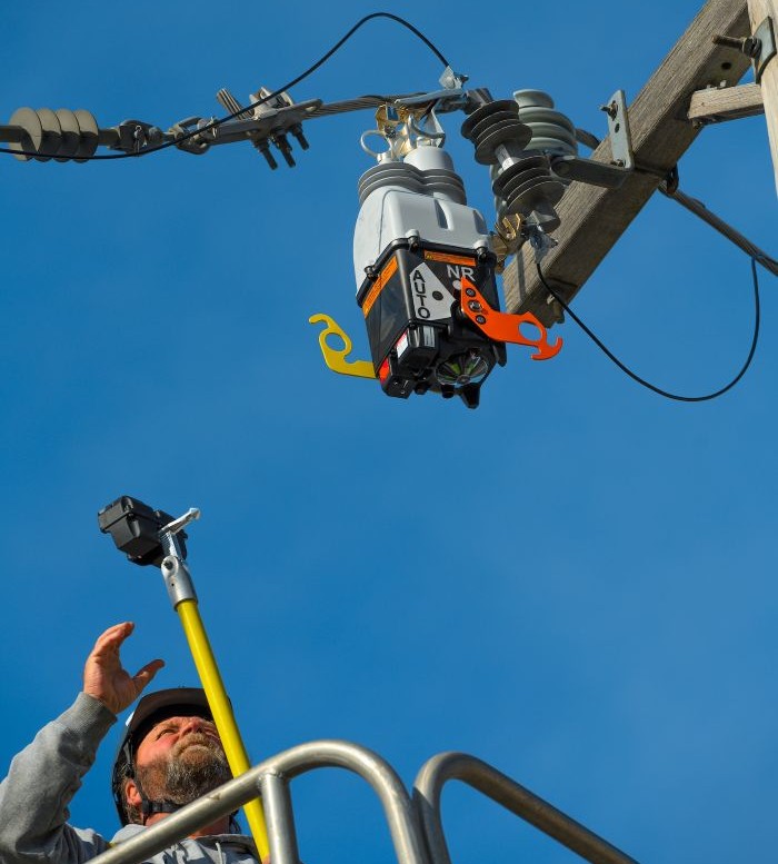 Lineworker inspecting an automated distribution device mounted on a utility pole as part of grid preparedness and maintenance efforts.