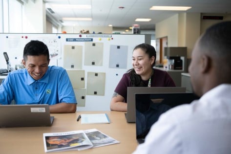 Three team members smiling and collaborating on their laptops